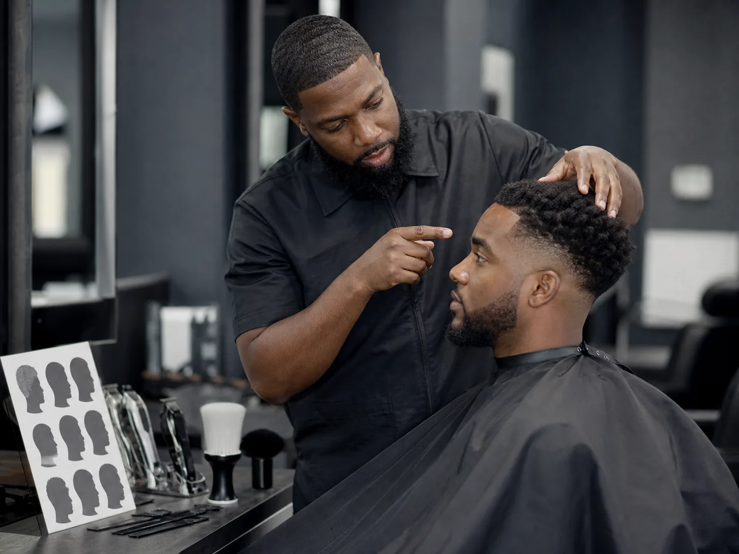 How to discuss a 90s-inspired hairstyle with a barber Anonymous Black barber discussing temple, fade height and top shape with a seated Black male client before cutting